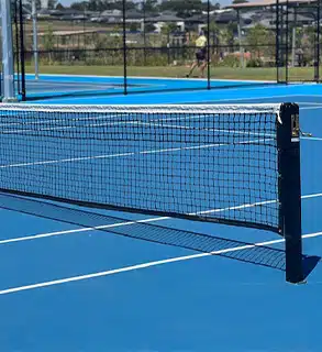 Sunny Day at a Modern Outdoor Tennis Court - RMA Sport Close-up of a tennis net on a bright blue outdoor hard court under sunny skies.