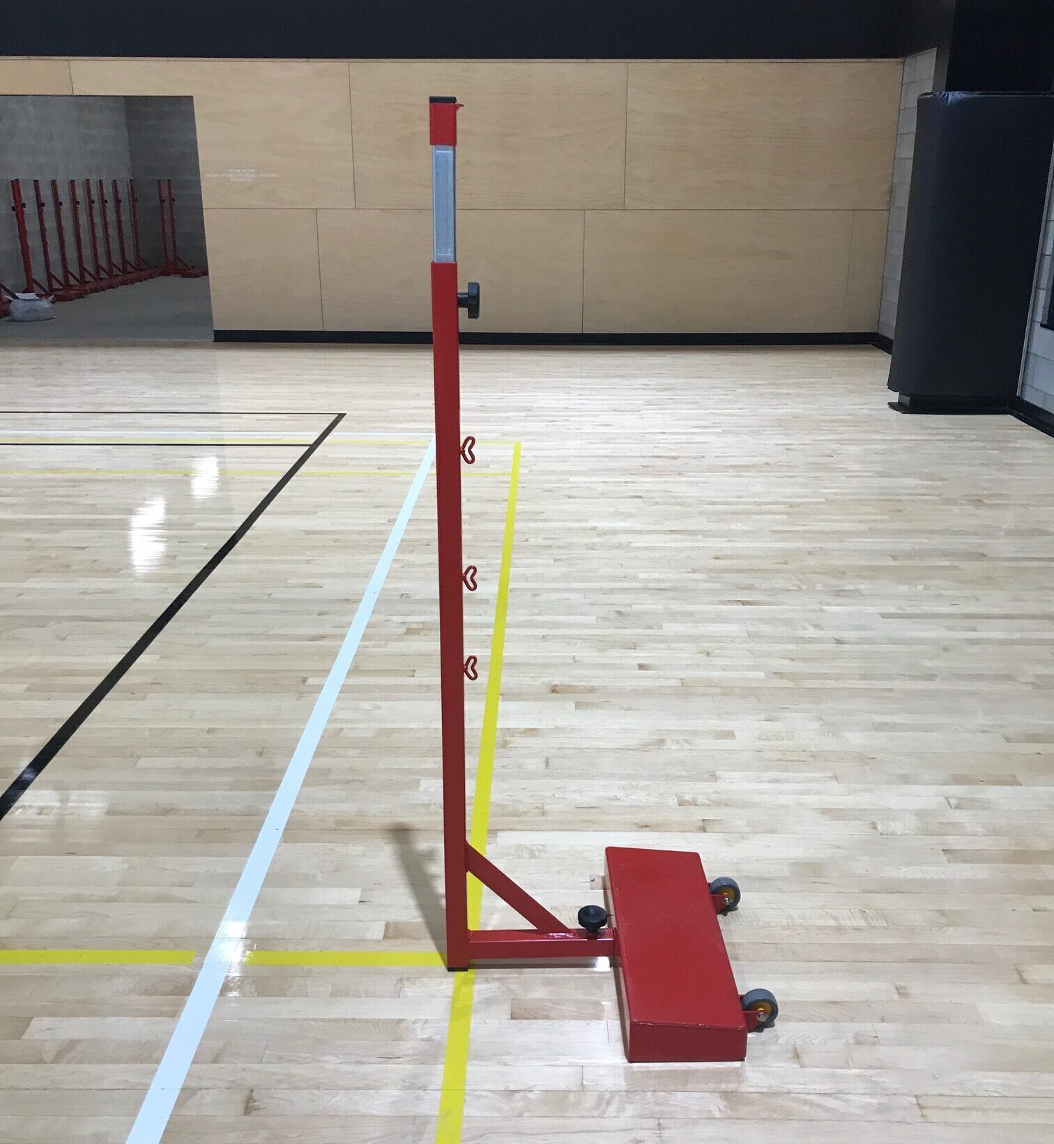 Red freestanding badminton post with wheels on indoor timber court
