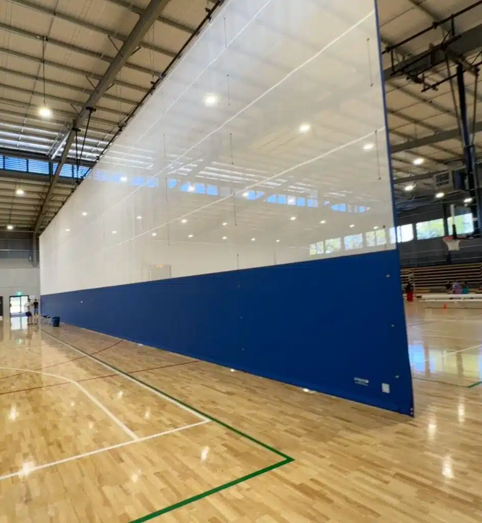 Essentials Curtain - RMA Sport Indoor gym with a tall white partition wall (blue lower panel) dividing the space into courts.