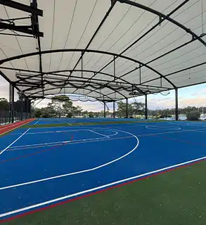 Covered Multi-Sports Court View – RMA Sport Installation - RMA Sport Covered outdoor basketball and tennis court with blue synthetic turf under a tensile roof structure
