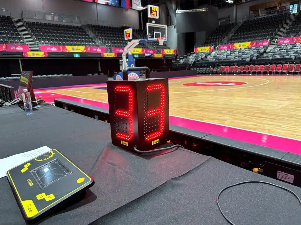 SB-TFD 2 - RMA Sport Close-up of a red LED timer on a black Bodet unit at the edge of a basketball court in an empty arena.