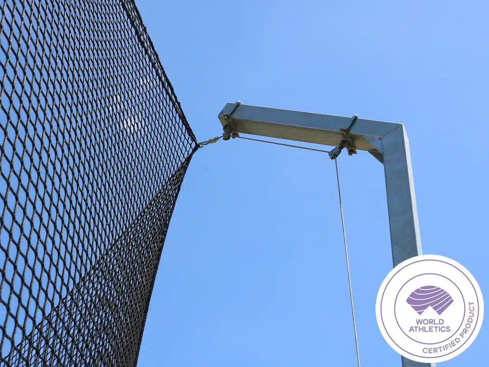 ATH-DTC64 - world-athletics-certified-competition-discus-throw-cage-2 - RMA Sport Close-up of a chain-link fence attached to a metal support post against a clear blue sky; World Athletics certified product badge in the lower-right corner.