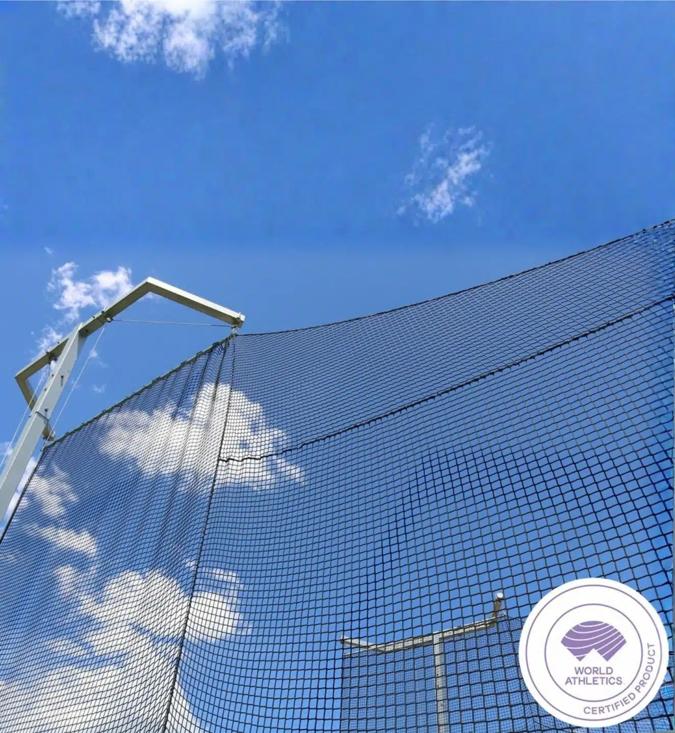 World Athletics Discus Cage - RMA Sport Blue sky with a white metal frame and a chain-link fence, featuring a World Athletics certified product badge in the bottom right.